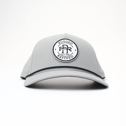 Rugged Refined rope hat with a structured front panel, featuring a circular black and white logo patch that reads "Rugged Refined Est. 2024." The hat has a black rope detail along the brim and perforated side panels for breathability.