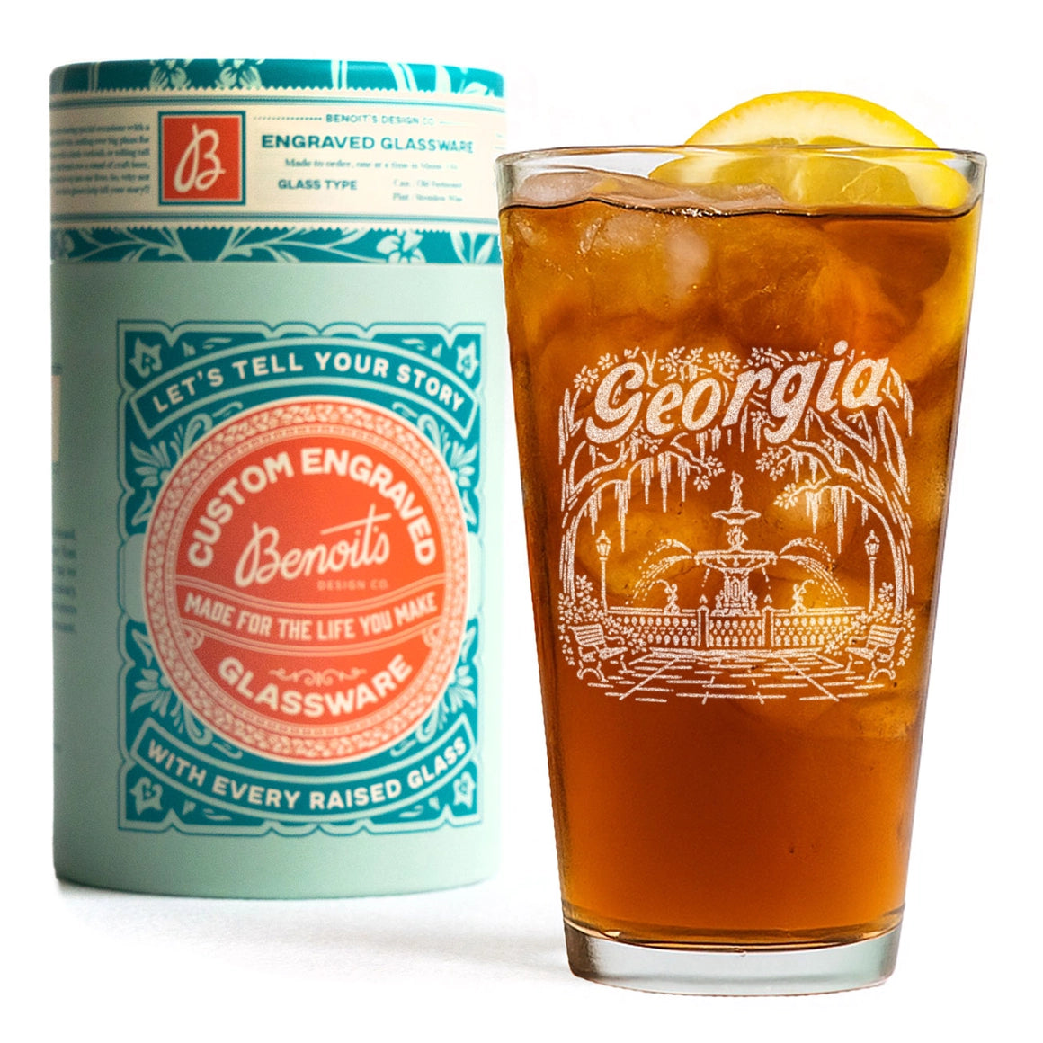 Benito brand engraved glassware set, featuring a light blue cylindrical packaging canister with teal and orange branding next to a clear glass filled with iced iced coffee and a lemon slice, showcasing the white floral engraving on the glass.