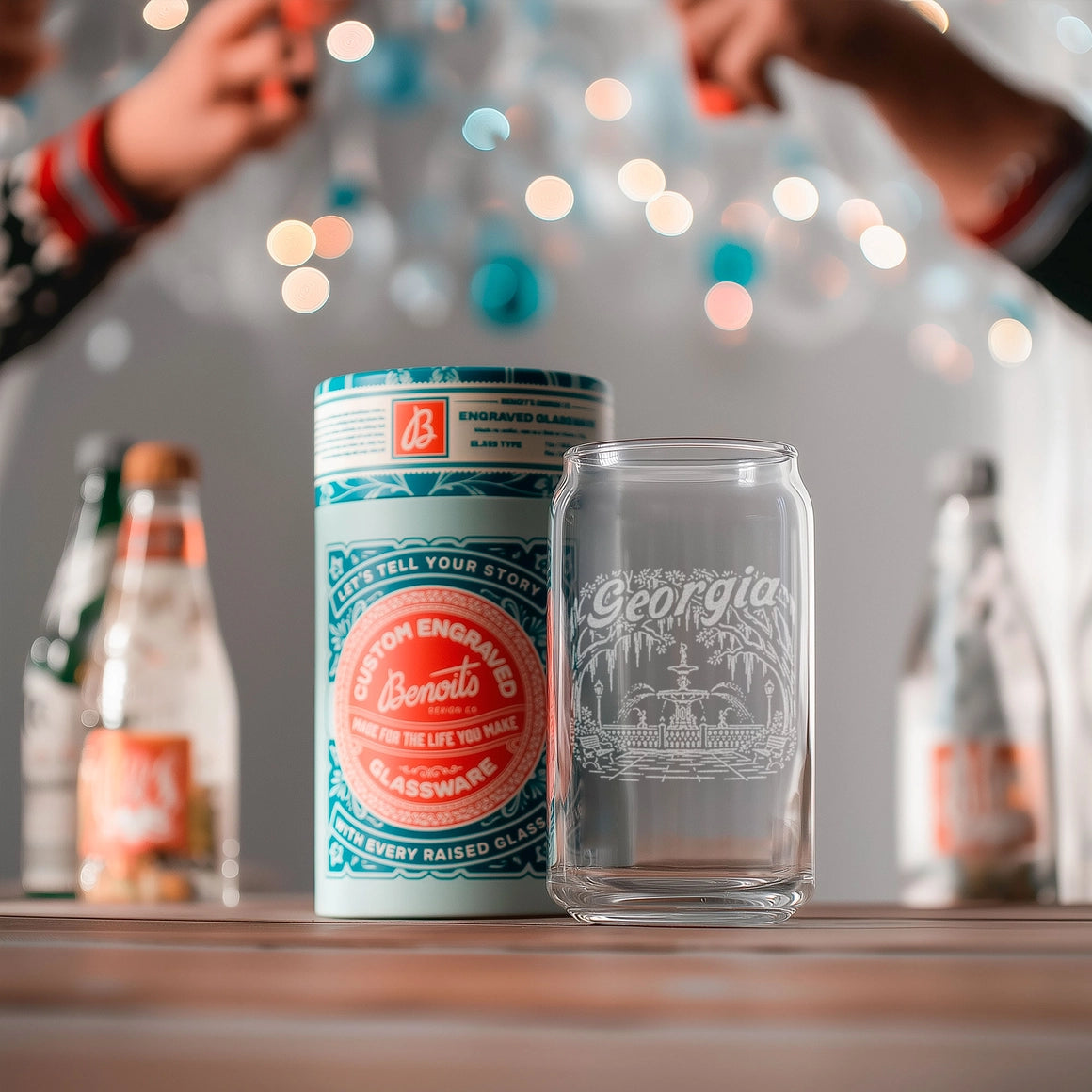 Canister and glass with engraved design on a wooden surface, blurred lights in the background